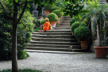 Femme assise sur des marches en pierre dans un parc luxueux. Femme en orange dans les jardins des...