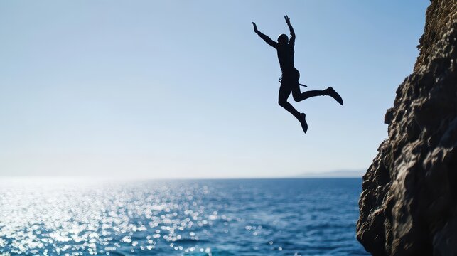 A person joyfully leaps off a cliff into the ocean, embodying adventure and freedom against a stunning blue sky.