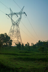 Tall electricity pylon stands tall against a vibrant sunset sky, overlooking a vast green field.