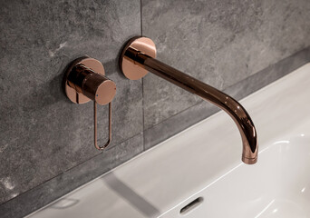 Copper coloured faucet. Wall-mounted faucet tap and lever handle: grey tiled wall, white sink,...