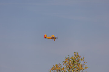 A small sport plane flies low over the ground. The sky is blue