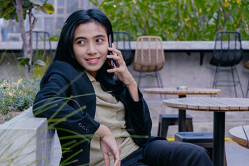 Fototapeta premium Smiling young businesswoman talking on cell phone in outdoor park.