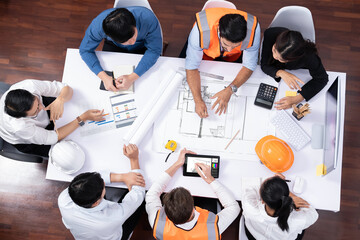 Top view banner of diverse group of civil engineer and client working together on architectural project, reviewing construction plan and building blueprint at meeting table. Prudent