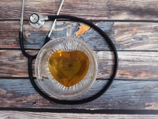 Heart shaped teacup with stethoscope on a wooden table, top view. Alternative medicine.