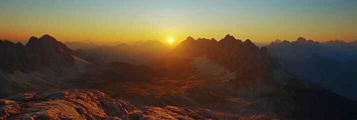 Naklejka premium Sunset amidst the mountains, panorama wallpaper, the beautiful light of the sun setting behind the horizon surrounded by mountains.