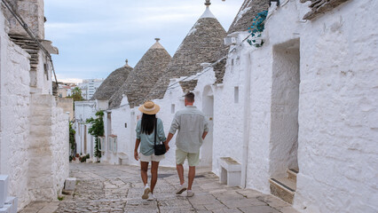 A couple walks hand in hand along the quaint, white-washed streets of Alberobello Puglia, Italy,...