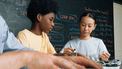 Young student fixing controller while teacher programing engineering code at STEM class. Closeup of...
