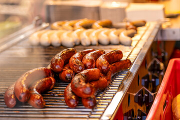 Close-up of different sausages on a barbecue grill handled by a person with barbecue tongs