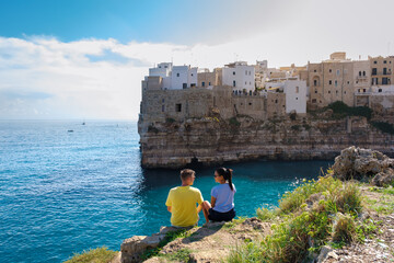 Polignano a Mare Overlooking the azure waters, a couple relaxes on a rocky outcrop in Puglia,...