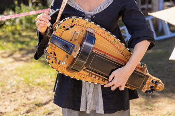 Musician is holding a hurdy gurdy while standing in a field during a medieval festival
