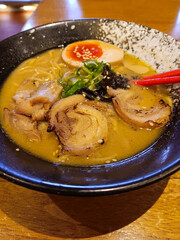 Miso tori paitan ramen with thick savory chicken broth, grilled chicken slices and egg in black bowl isolated on wooden table.