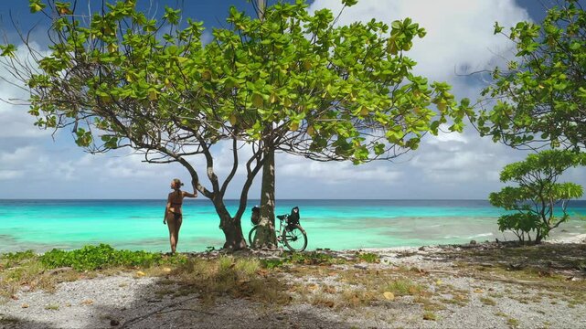 Young woman is taking a break from cycling around a tropical island, enjoying the turquoise waters and lush vegetation