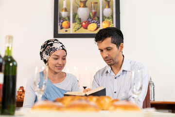 Smiling couple reading the torah during a Hanukkah celebration, with traditional sufganiyot donuts on the table and candlelight in the background, highlighting a joyful and intimate moment of faith.