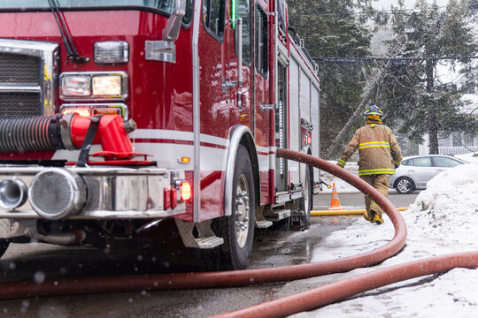 Fireman is walking through the snow pulling a large fire hose away from the firetruck during a snowstorm. Selective focus
