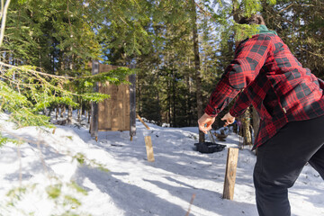 Lumberjack throwing an axe at a wooden target in a snowy forest, enjoying a traditional winter activity. Selective focus