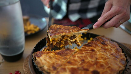 Hand cutting a slice of homemade savory pie, revealing a delicious filling of shredded chicken, corn, and vegetables, capturing the rich texture and golden crust in a warm, home-cooked setting