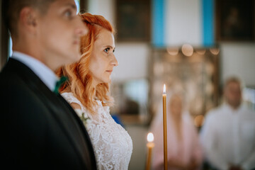 Bride and groom hold lit candles during a wedding ceremony, focusing on the bride’s solemn expression as soft light illuminates the scene..
