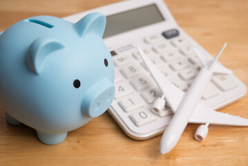 Blue piggy bank, airplane and white calculator on wooden table background. Travel budget, buying flight ticket and hotel booking, savings and money management for travel holiday, home finance concept.