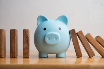 Piggy bank protect danger from domino effect on wooden table. Savings help from economy crisis...