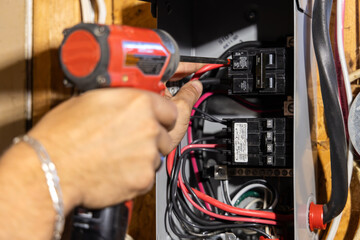 Electrician is installing a new circuit breaker in a residential electrical panel using a power drill. Selective focus
