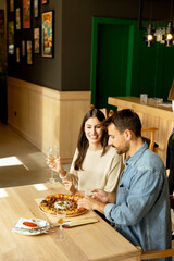 Couple enjoying a delightful meal at a cozy restaurant while sharing a delicious pizza and a glass of white wine