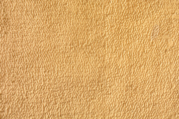 A tan wall with a textured surface. The wall is covered in a pattern of small dots