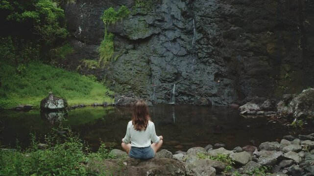 Woman practicing yoga near a small waterfall in a wild tropical jungle. She is enjoying a peaceful moment of mindfulness and connection with nature