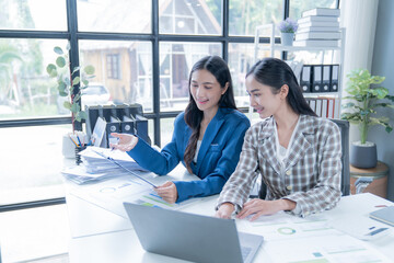 Two young businesswomen are having a productive meeting, analyzing financial data and using a laptop to enhance their workflow in a modern office environment