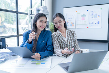 Two businesswomen are having a discussion while working together in their modern office. They are smiling and seem to enjoy their work