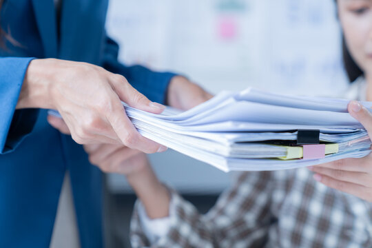 Two businesswomen collaborating in the office, passing paperwork. Working closely, sharing responsibilities, showing teamwork. Close-up of hands exchanging files, demonstrating dedication and trust