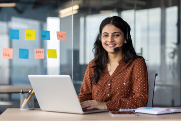 Smiling woman with headset working on laptop in office. Customer service concept. Professional...