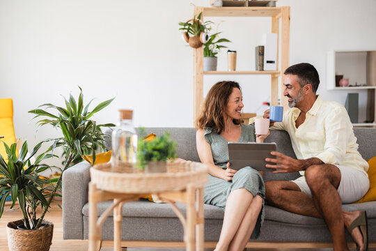 Couple relaxing on sofa using digital tablet and drinking coffee at home