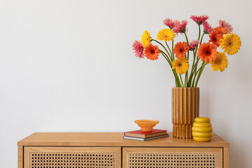 A cheerful arrangement of orange and yellow gerberas in a wooden vase on a rattan-front sideboard. Bright and bold, yet elegant.