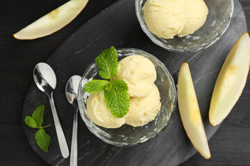 Scoops of melon sorbet with mint in glass dessert bowls, fresh fruit and spoons on dark wooden table, flat lay