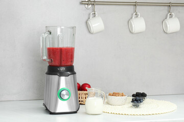 Blender with mixture of ingredients and other fresh products on white countertop in kitchen