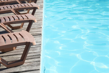 Fototapeta premium Empty sun loungers on wooden deck near outdoor swimming pool