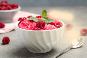 Delicious raspberry sorbet with fresh berries in bowl and spoon on gray textured table, closeup