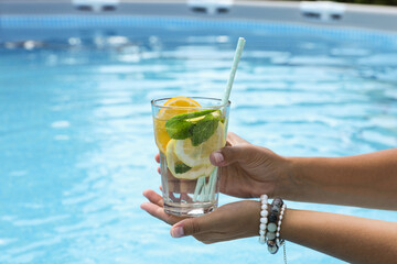 Woman holding tasty cocktail in glass near swimming pool outdoors, closeup