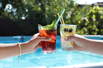 Women holding tasty cocktail in glass near swimming pool outdoors, closeup