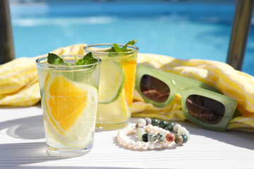 Tasty cocktail in glasses and sunglasses near swimming pool outdoors