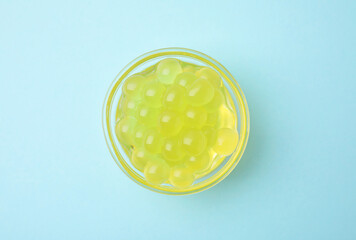 Bright tapioca pearls in bowl on light blue background, top view