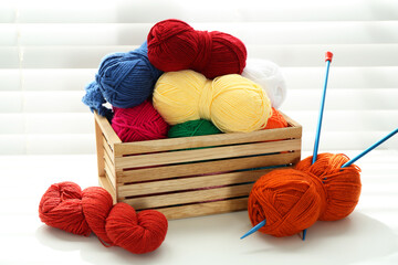 Skeins of soft yarn in crate and knitting needles on white table indoors