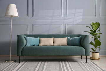 Comfortable sofa, houseplant and lamp near grey wall in room