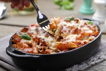 Woman eating delicious al forno pasta at wooden table, closeup