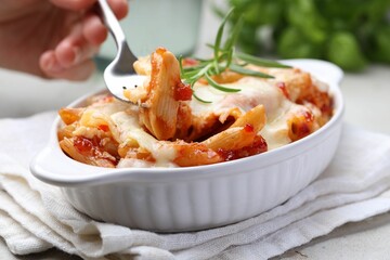 Woman eating delicious al forno pasta at light table, closeup