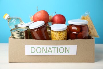 Different food products for donation in box on table against light blue background