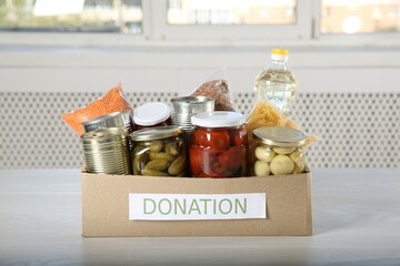 Different food products for donation in box on wooden table indoors