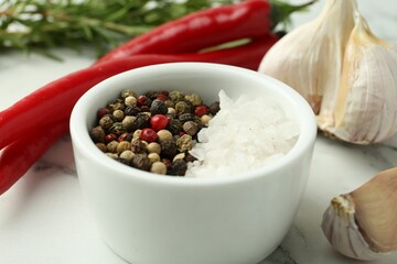 Sea salt, peppercorns, chili peppers and garlic on white marble table, closeup