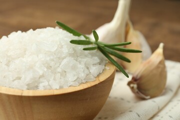 Sea salt in bowl, rosemary and garlic on brown table, closeup