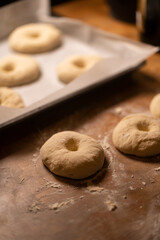 Dough shaped in bagels with flour on a wooden desk, pan with buns ready for baking 